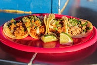 four tacos on a pink plate with lime wedges